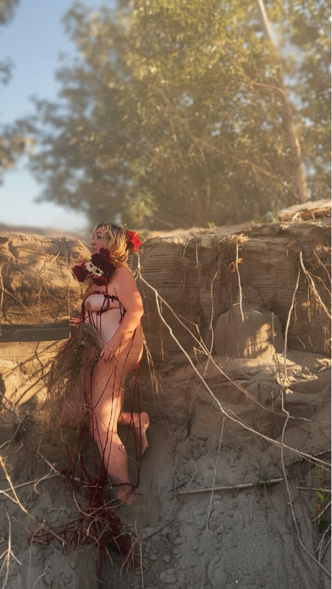 Red Thread, further work. Standing against an eroded sand bank among exposed roots, wound in red thread and roses.