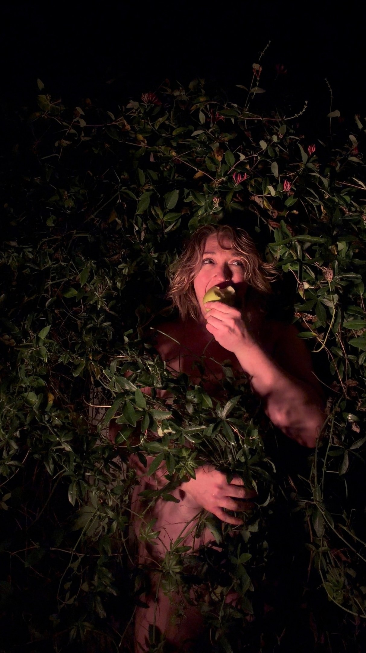 Fear Not, 4 of 6. Biting a green apple among the vines, eyes raised, one hand low against the body.