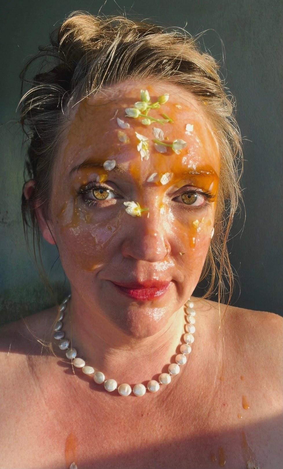 Taste and See, 4 of 5. Facing the camera with a direct gaze, the face covered in honey and petals, a pearl necklace.